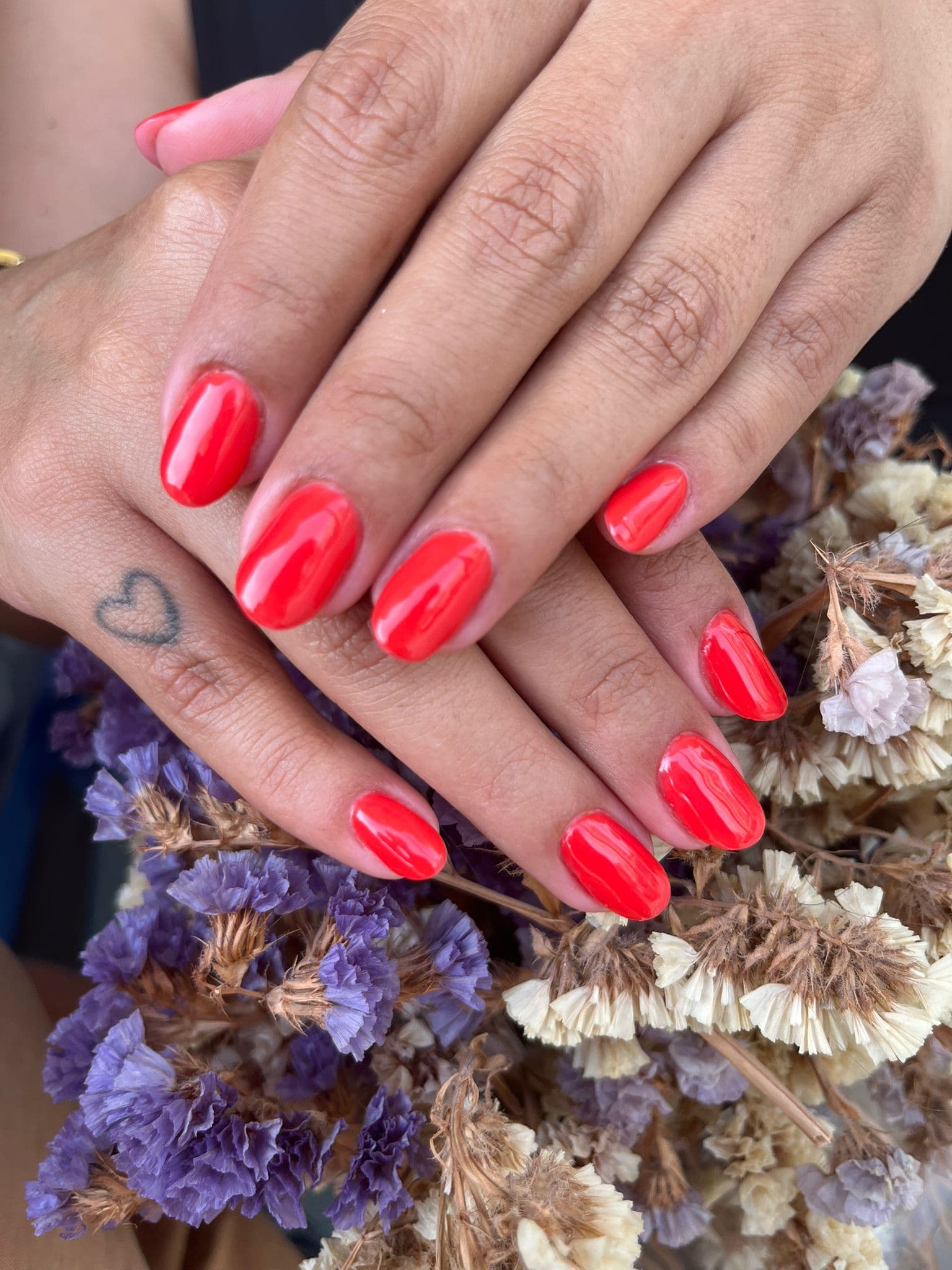 Manicure em tom coral vibrante feita pela Fah Salviano, com flores secas ao fundo